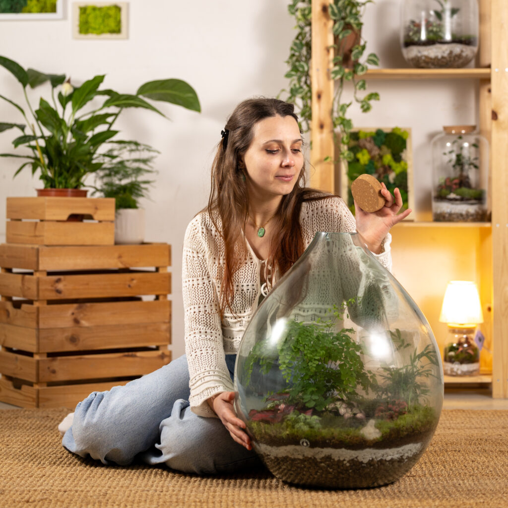 ragazza crea un terrario artigianale damigiana in vetro con piante verdi in casa